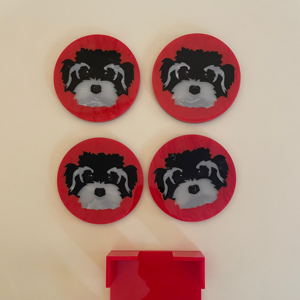 Four red circular coasters featuring a black and white dog face design, arranged above a red rectangular tray on a light beige background.